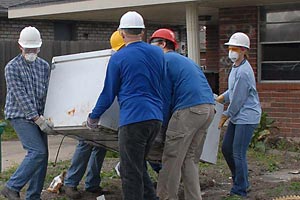 Volunteers carrya refrigerator out to the curb for disposal.