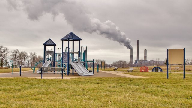 A plume of emissions rises from a factory smokestack near an empty playground
