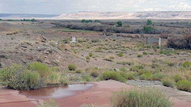 Desert vista with "Warning: Keep Out" sign, concrete wall in mid photo and concrete pad in foreground