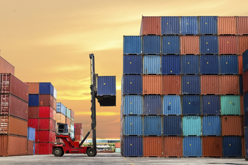 A photograph of a reach stacker moving a container in a container yard.