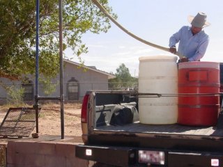 Man filling up water drums at water hauling station in Ganado