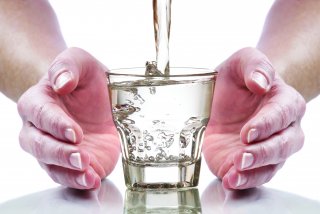 Hands around clean safe drinking water flowing from the tap into a glass
