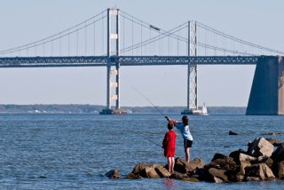 Photo of 2 people casting rods on the shores overlooking the bay bridge.