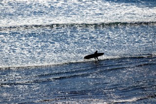 silhouette of person carrying surfboard through shallow water along the coast 