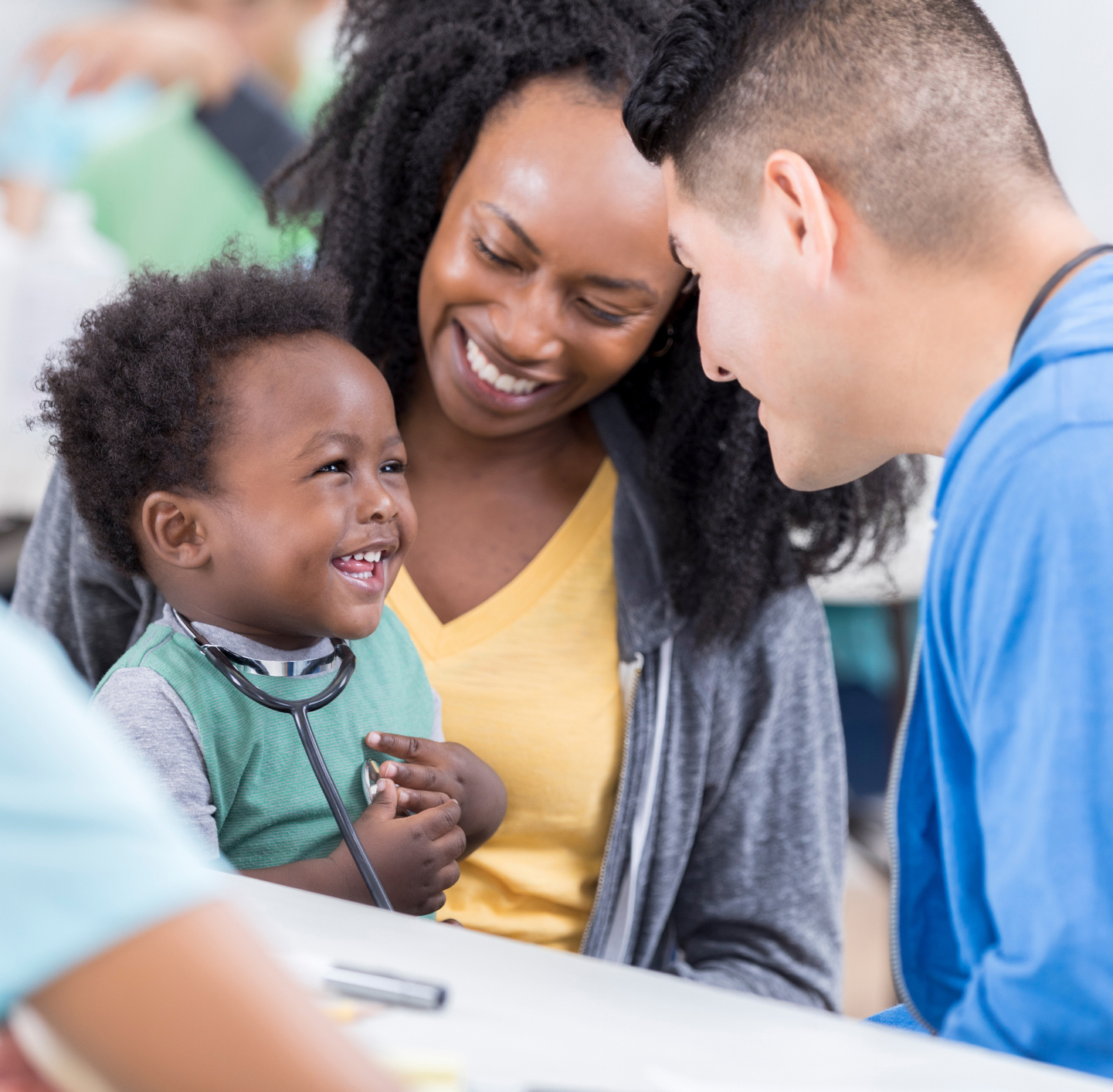 child with stethoscope on Doctor's chest with adult in background