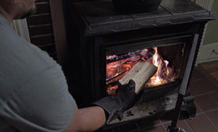 a man placing split wood into a burning woodstove