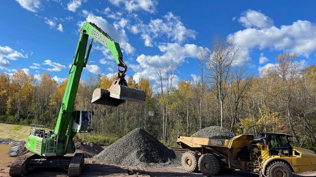 An excavator unloads armor stone for capping operations. 