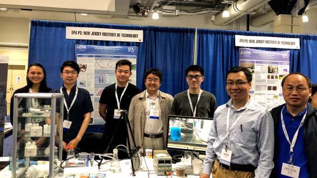 Seven smiling New Jersey Institute of Technology faculty and students posing in front of their project for removing PFOS