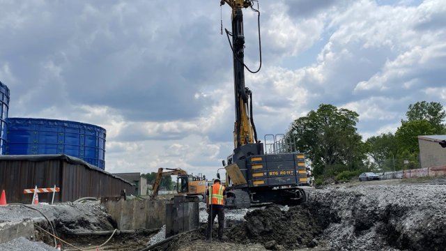 A machine drives sheet piling into the ground along the south track