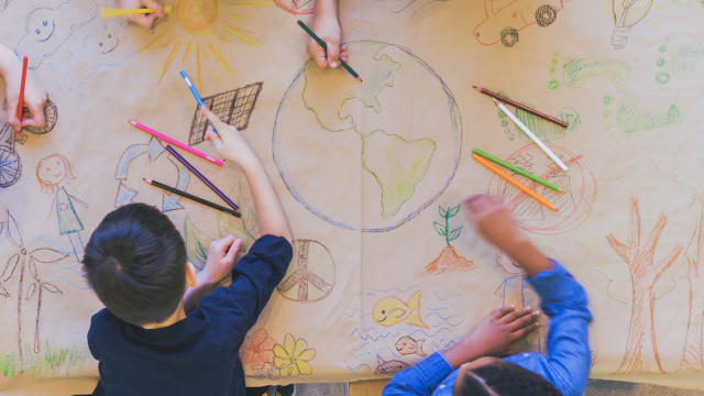 Six children drawing a glob on a large sheet of paper.