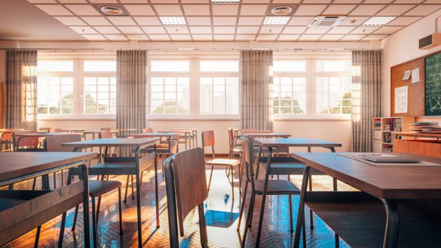 Inside of a classroom with desks and a chalkboard in the distance.