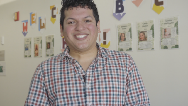 A male EPA employee wearing a buttoned-down shirt standing in front of a white wall with posters being displayed.