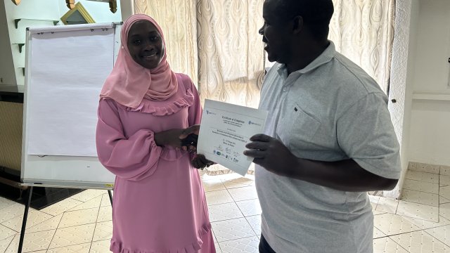 Woman in pink dress smiling at camera and receiving a certificate of completion from man wearing white polo top.