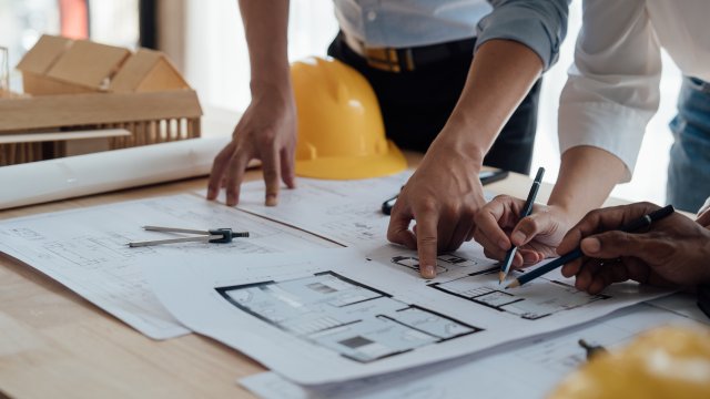 Three construction workers at a table overlooking drawings at a construction site.