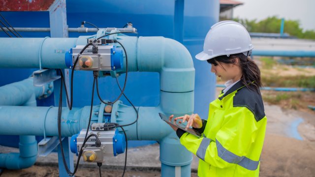 Woman engineer, in yellow safety vest and white hard hat, works at wastewater treatment plants.