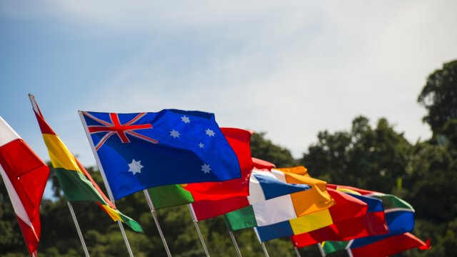 Row of flags of multiple countries flying against a blue sky