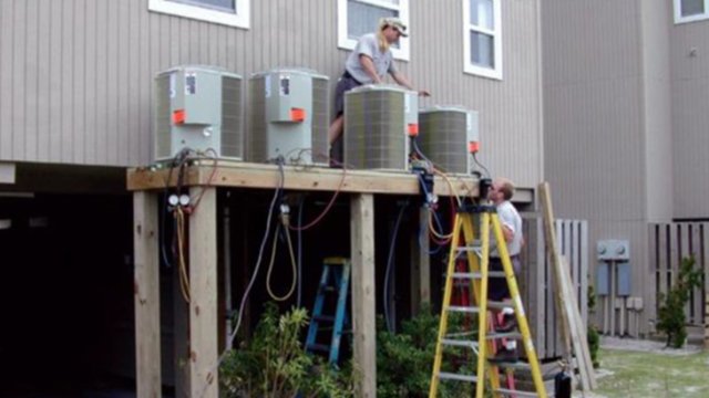 worker standing on a platform with air conditioning units to prevent flooding in a coastal area 