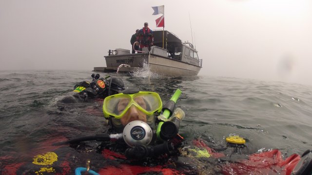 EPA diver in full SCUBA gear floating in open water behind boat.