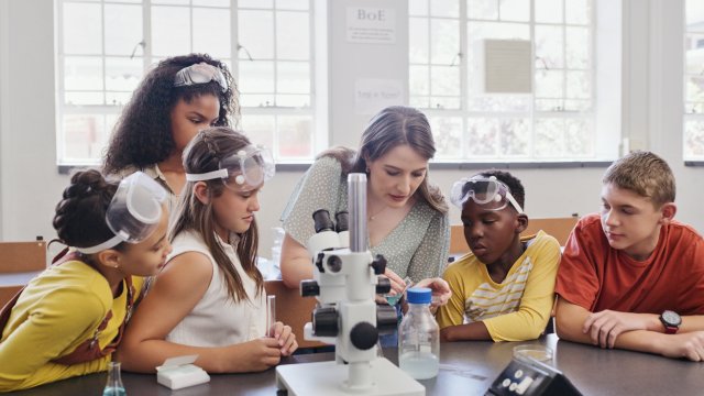 image of students gathered around teacher in a science lab using a microscope