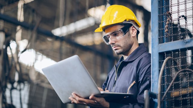An engineer wearing a yellow hardhat while looking at a computer