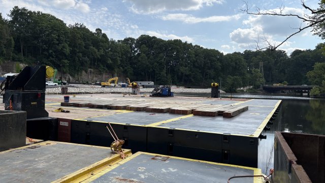 Large platform floating in river water with construction equipment in the background.