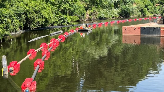 Pipes float on top of water. Some of the pipes have red cylindrical floats on them. 