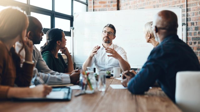 Five people in a meeting with a whiteboard in the background