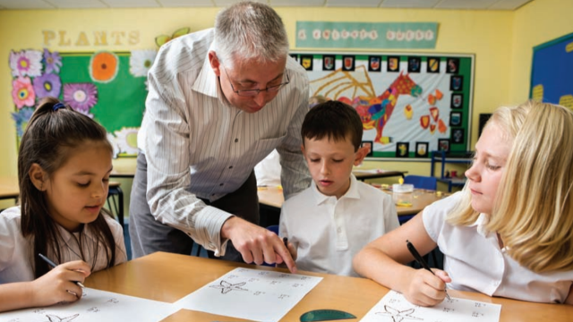 Three students working on an assignment in a classroom with their teacher