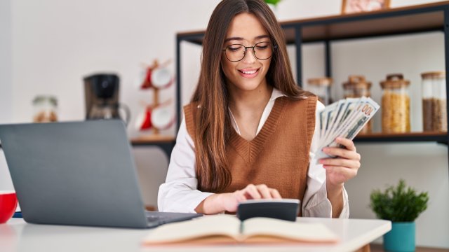 A woman in front of a computer with money in her hand.