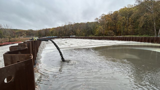 Muddy water pours out of a pipe on top of sheetpile wall into a pool of water. 