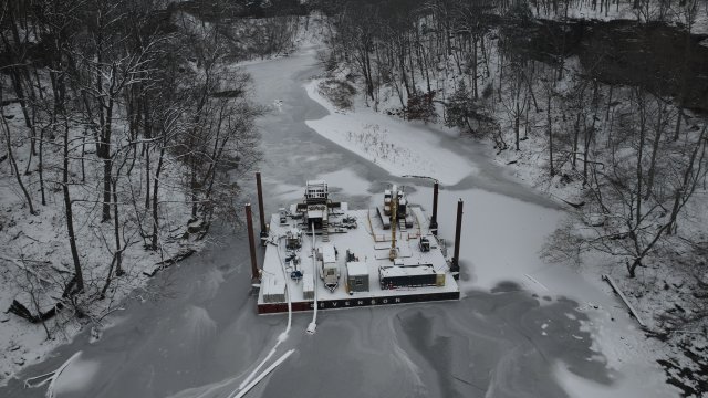 Floating platform in the middle of an ice-covered river with construction equipment on it. 