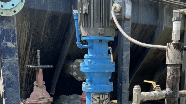 A large blue piece of machinery attached to a black steel pipeline. The blue machinery has a large sticker on it that says “Super Shredder.”
