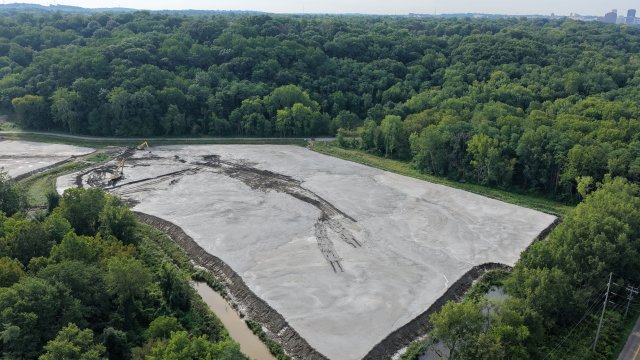  A birds-eye view of a large clearing filled with flat, gray soil, surrounded by a lush green forest.