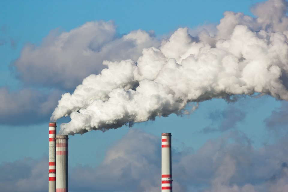 Three industrial smokestacks with white-colored emissions coming out of them.