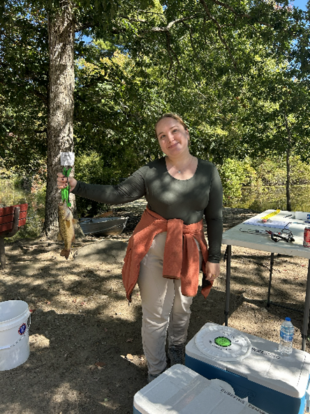 A woman holding a fish with trees in the background.