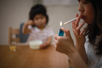 a person lighting a cigarette with a baby looking on in the background