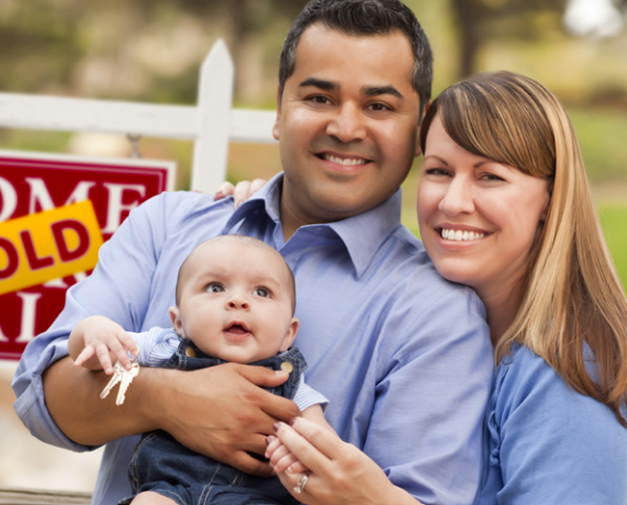 Family standing in front of a for sale sign