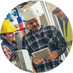 three workers in hardhats conversing, while one holds a clipboard
