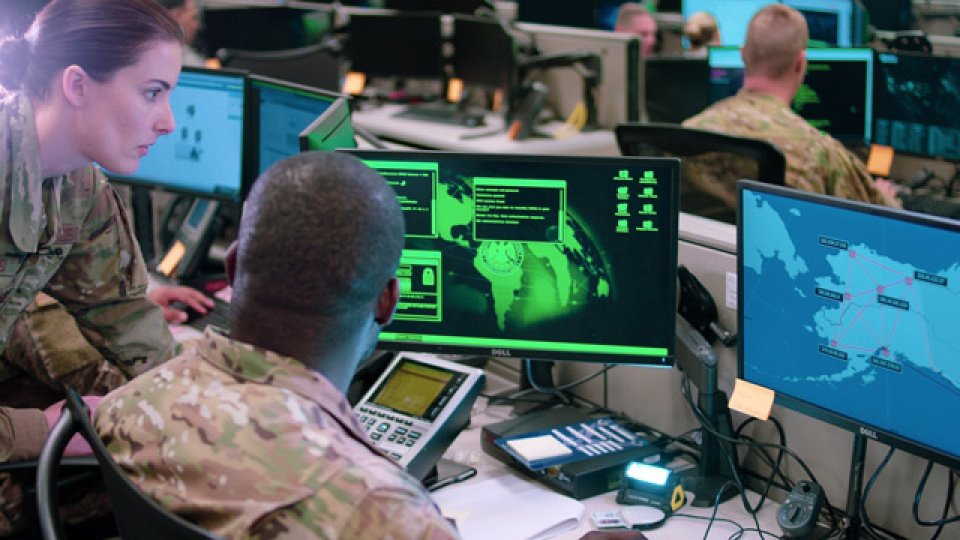 Two armed services personnel look at a map on a computer screen.