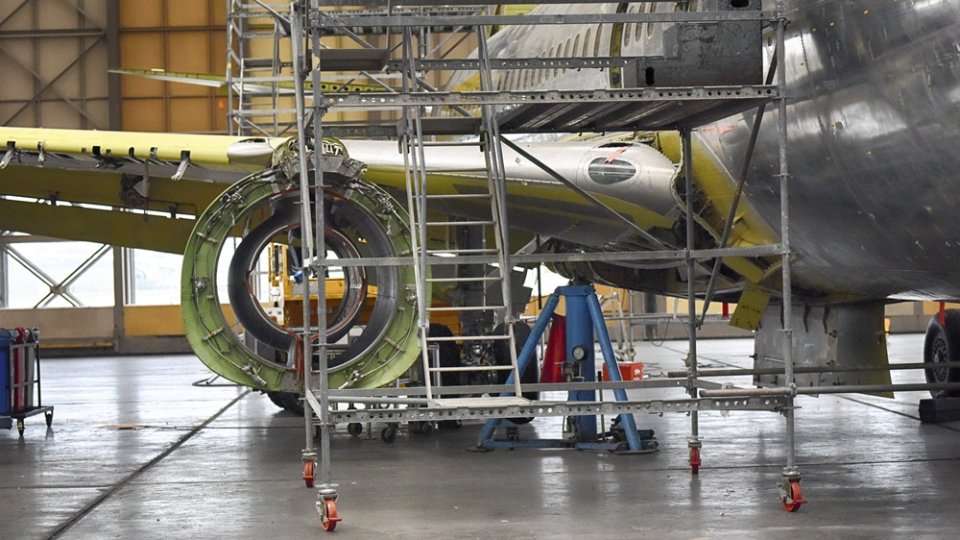 An airplane under construction in a hangar with scaffolding nearby.