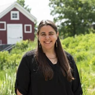 woman smiling standing in a field with a house in the background