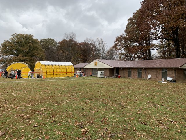 OTECRA field study site includes a one-story building with a grassy front lawn. Responders set up a yellow tent for a decontamination line in front of the building.