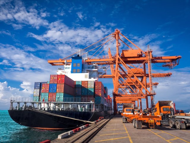 A large shipping vessel with containers onboard next to a port dock with large cranes.