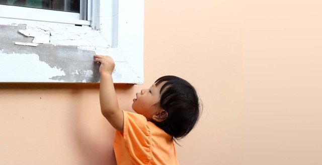 young child is playing with paint chipping off window sill.