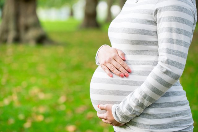 A pregnant woman holds her stomach in profile