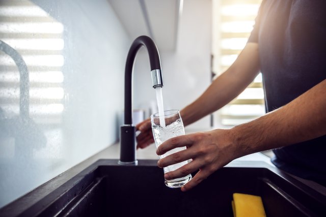 person filling glass with water from a faucet