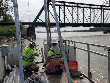 Two workers on a boat collect sediment samples along the Lower Maumee River at the Sway Bridge Project Area during predesign investigation. 