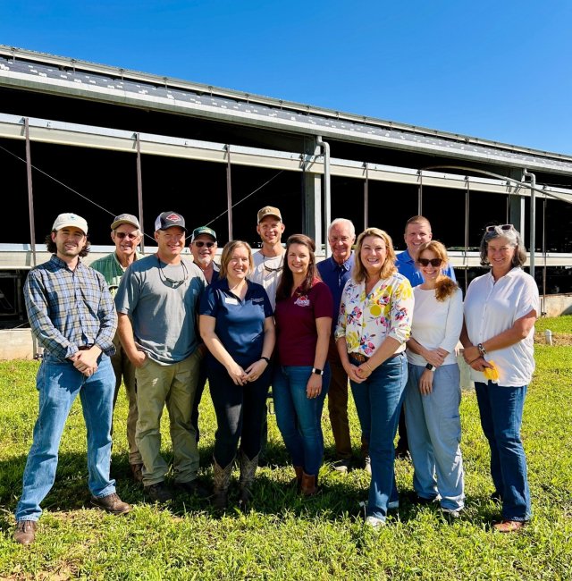 Smiling EPA staff, partners, and farmers in front of a diary farm on a summer day. 