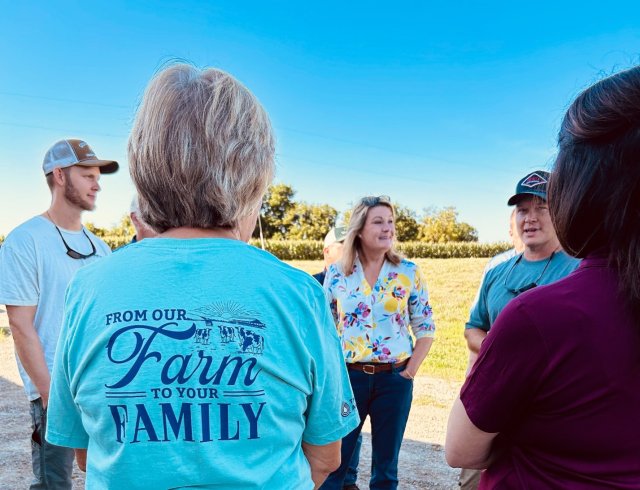 EPA R3 Regional Administrator talks to partners outside a dairy farm on a summer day, with a woman wearing a shirt that says, "from our farm to your family". 