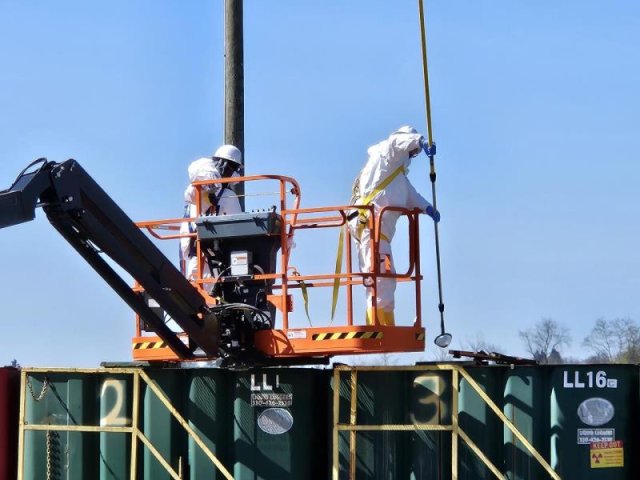 Two workers in haz-mat gear stand on an aerial lift over frac tanks to collect samples at the Fairmont Brine Site.
